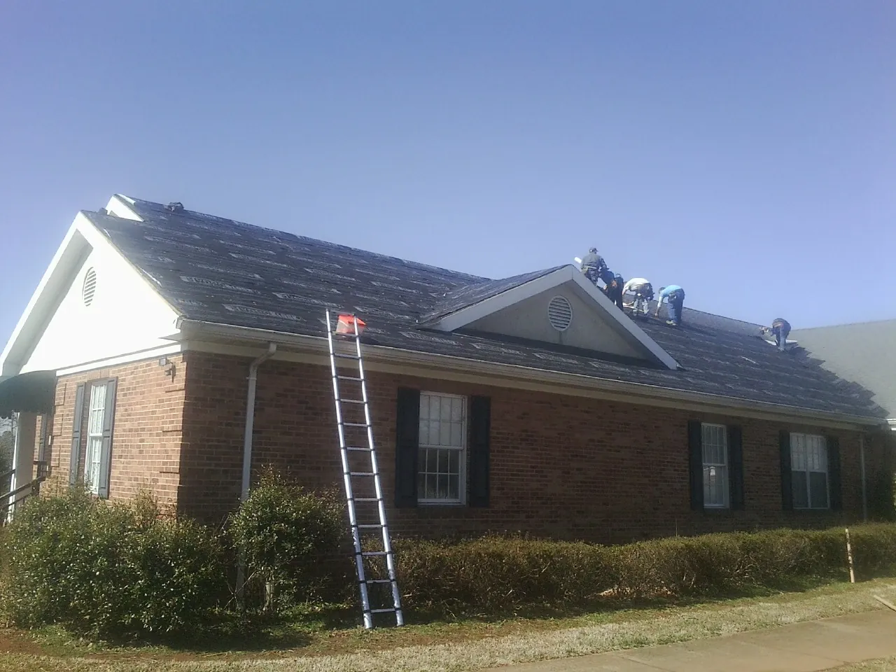 Crew tearing shingles off a brick ranch roof with a ladder set — Metal Roof Repair work by our crew in Earlville