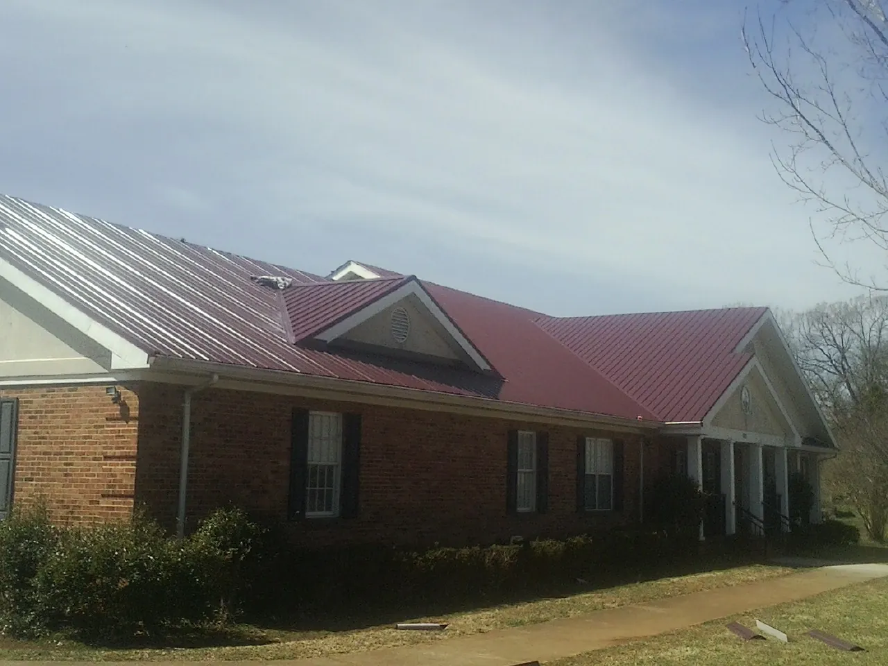 Red metal roof with gabled entries on a long brick building, from a Hail Damage Roof Repair job in Earlville