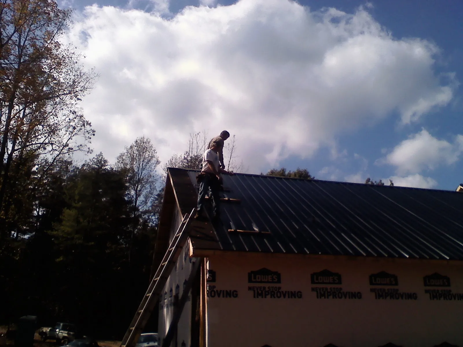 Roofer fastening dark metal panels high against a cloudy sky, from a Roof Inspection job in Earlville