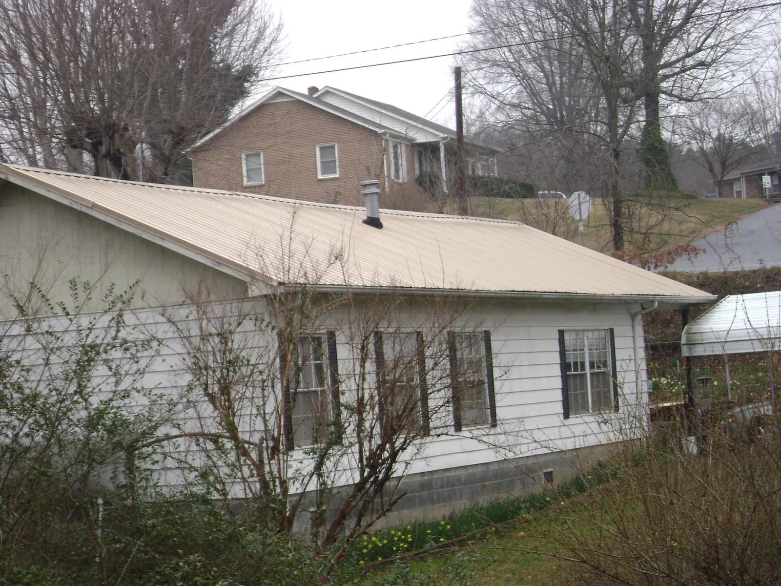 Tan metal roof on a white sided house set into a hillside — Commercial Roofing by Roofing Brothers in Earlville