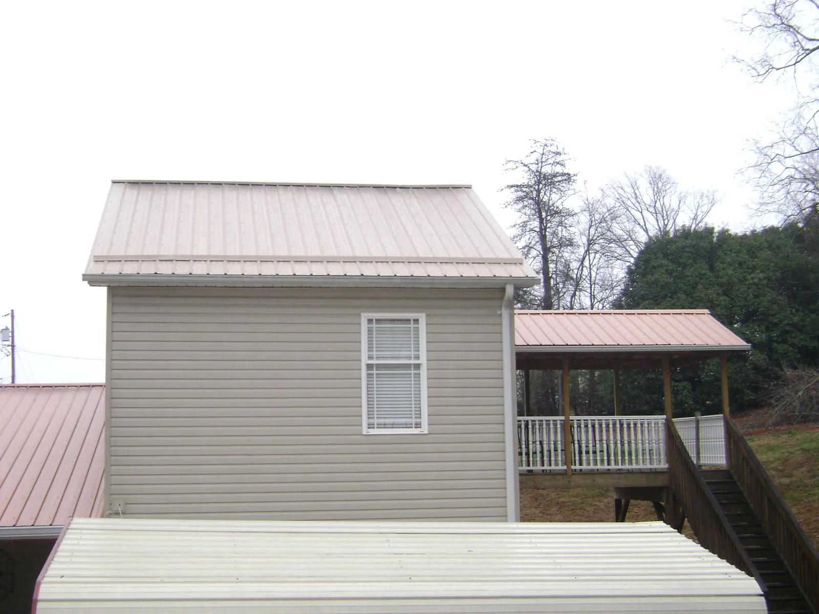 Tan metal roofs on a two story addition and attached porch, from a Roof Replacement job in Earlville